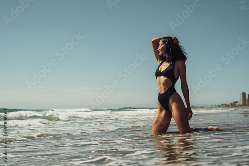 beautiful brunette girl in a black swimsuit on the seashore stands in the water