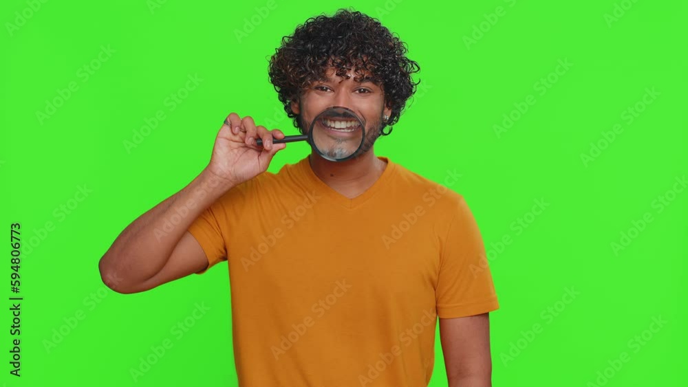 Indian man holding magnifier glass on healthy white teeth, looking at camera with happy expression, showing funny silly face smiling mouth. Handsome hindu guy isolated on green chroma key background Indian man holding magnifier glass on healthy white teeth, looking at camera with happy expression, showing funny silly face smiling mouth. Handsome hindu guy isolated on green chroma key background