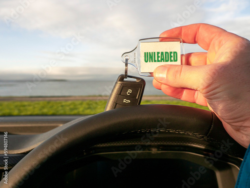 Driver holding car key with unleaded badge. Beautiful nature scene with ocean and mountain out of focus in the background. Travel or trip in rented car concept.