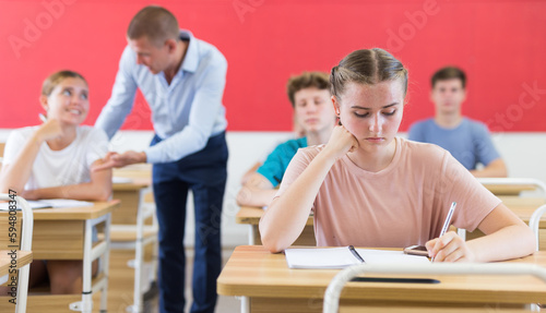 Portrait of focused teenage schoolgirl writing lectures in workbooks in classroom during lesson..