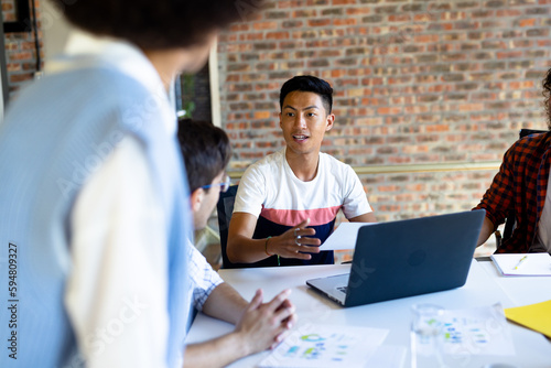 Busy diverse creative colleagues using laptop and discussing project at design meeting photo