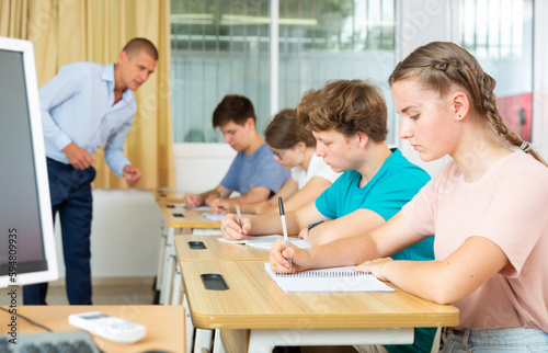 Teenagers listening to lecturer and writing in notebooks in classroom