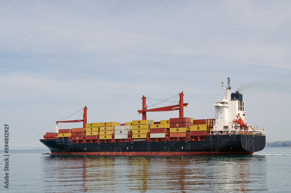 Cargo ship filled with containers on the sea, against the background of the coastline. Transportation of goods by sea Cargo ship filled with containers on the sea, against the background of the coastline. Transportation of goods by sea