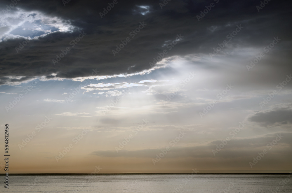 Calm sea, horizon, sun behind the clouds, beautiful sunbeams from behind the clouds