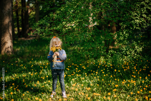 A girl walks through the woods in a clearing with a bouquet of yellow dandelions in her hand