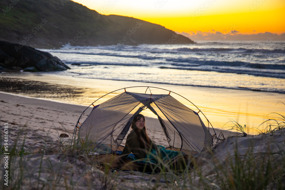 A beautiful girl admires a wonderful sunrise on the beach from her tent. Camping on the beach in Australia, Hat Head National Park, NSW