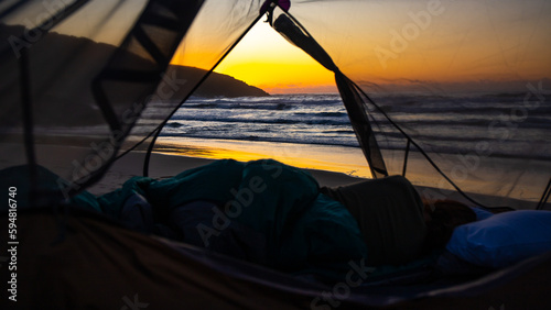 A beautiful girl admires a wonderful sunrise on the beach from her tent. Camping on the beach in Australia, Hat Head National Park, NSW