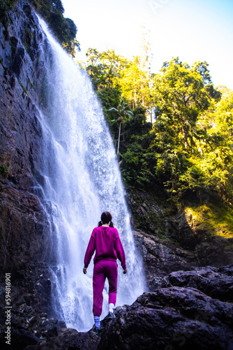 close up on a beautiful, brave, long haired girl standing in front of a large waterfall in australian rainforest, red cedar falls in dorrigo national park, new south wales, between brisbane and sydney photo