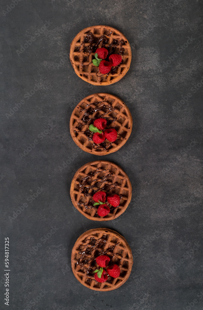 Vegan small Round chocolate waffles with and raspberries.  Dark gray background. Top view