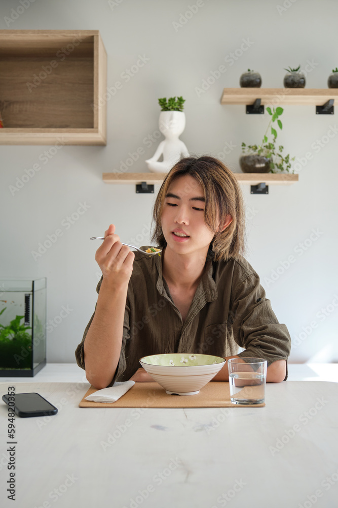 Smiling taiwanese young man eating soup in the living room. Having lunch. Smiling taiwanese young man eating soup in the living room. Having lunch.