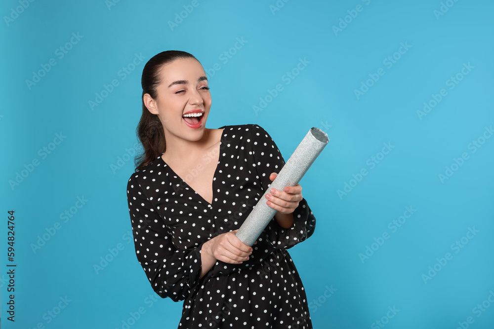 Young woman blowing up party popper on light blue background Young woman blowing up party popper on light blue background