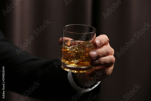 Man holding glass of whiskey with ice cubes on dark background, closeup