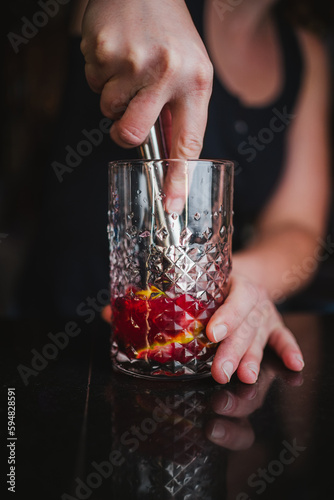 Woman mashing limes and berries in a glass using a muddler to make a fruit mojito in a bar