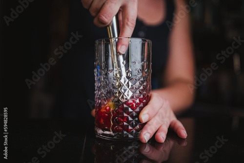 Woman bartender mashing limes and berries using a muddler to make a fruit mojito in a pub bar photo
