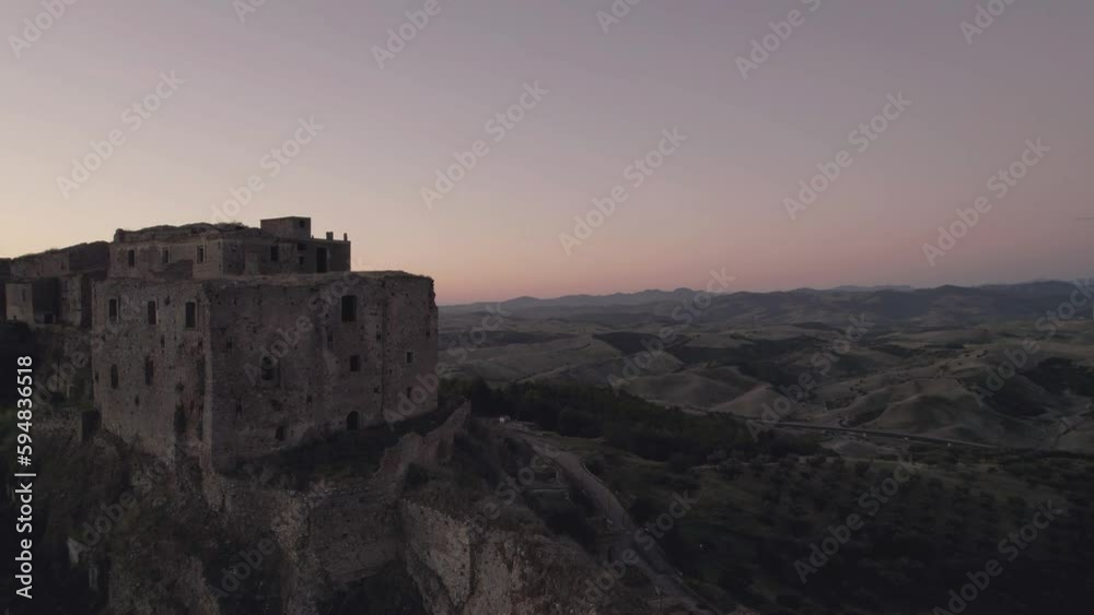 Drone flying in circulair motion around the ruins of Craco in the south of Italy in the very early morning sunrise in 4k