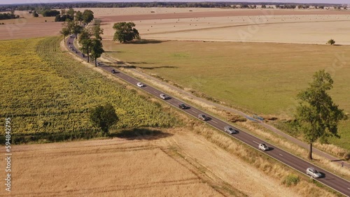 A diagonal descent of a drone across a busy country road to a meadow with a view of wide fields. Location: Brandenburg, Germany in summer