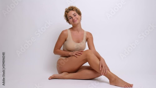 Young happy girl in bust bodice sits on the floor against white background, smiling happily sexy model in beautiful pose indoors, relax concept, copy space, high quality video