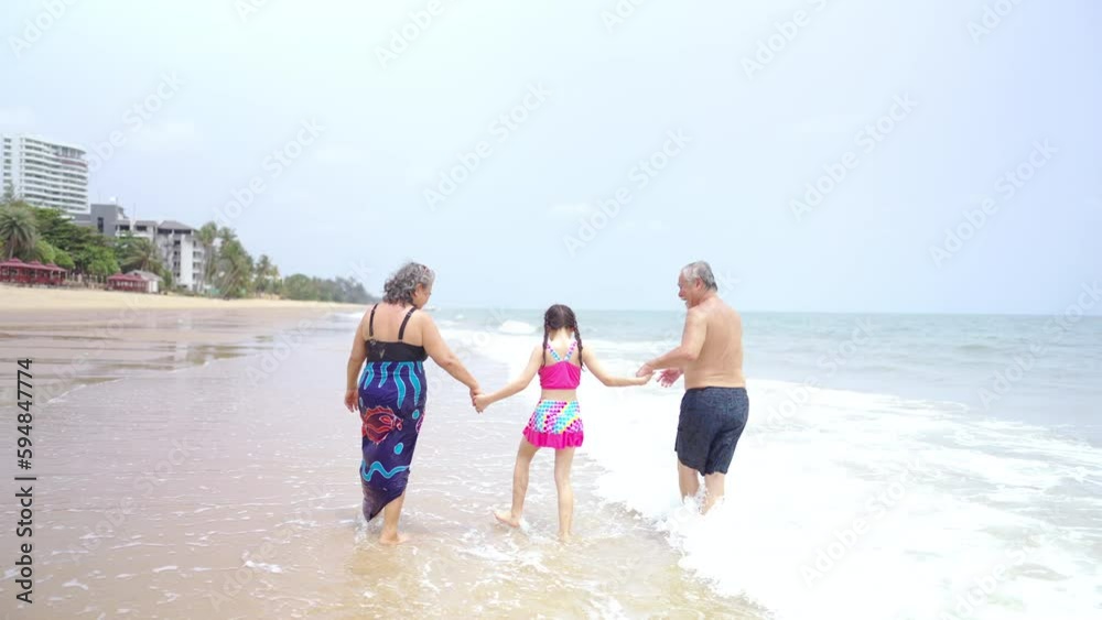 4K Happy Asian family travel ocean on summer holiday vacation. Grandparents and grandchildren girl in swimwear enjoy and fun outdoor lifestyle playing sea water together at tropical beach in sunny day 4K Happy Asian family travel ocean on summer holiday vacation. Grandparents and grandchildren girl in swimwear enjoy and fun outdoor lifestyle playing sea water together at tropical beach in sunny day