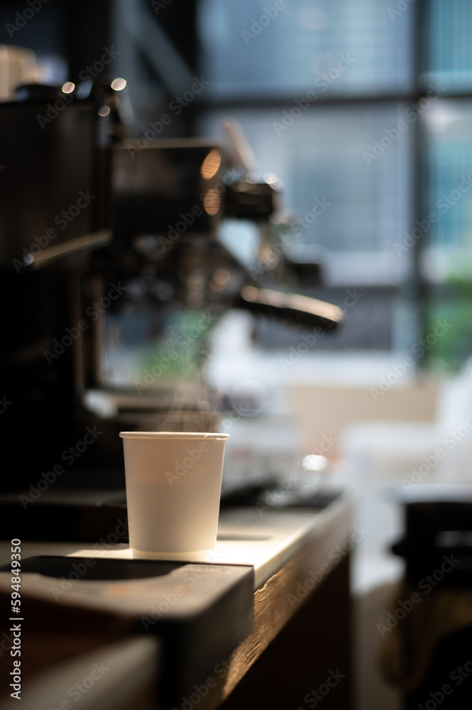 A cup of coffee sits on a table with a coffee machine in the background.