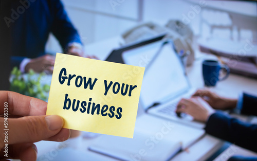 Male hand holding sticky note written Grow your business.
