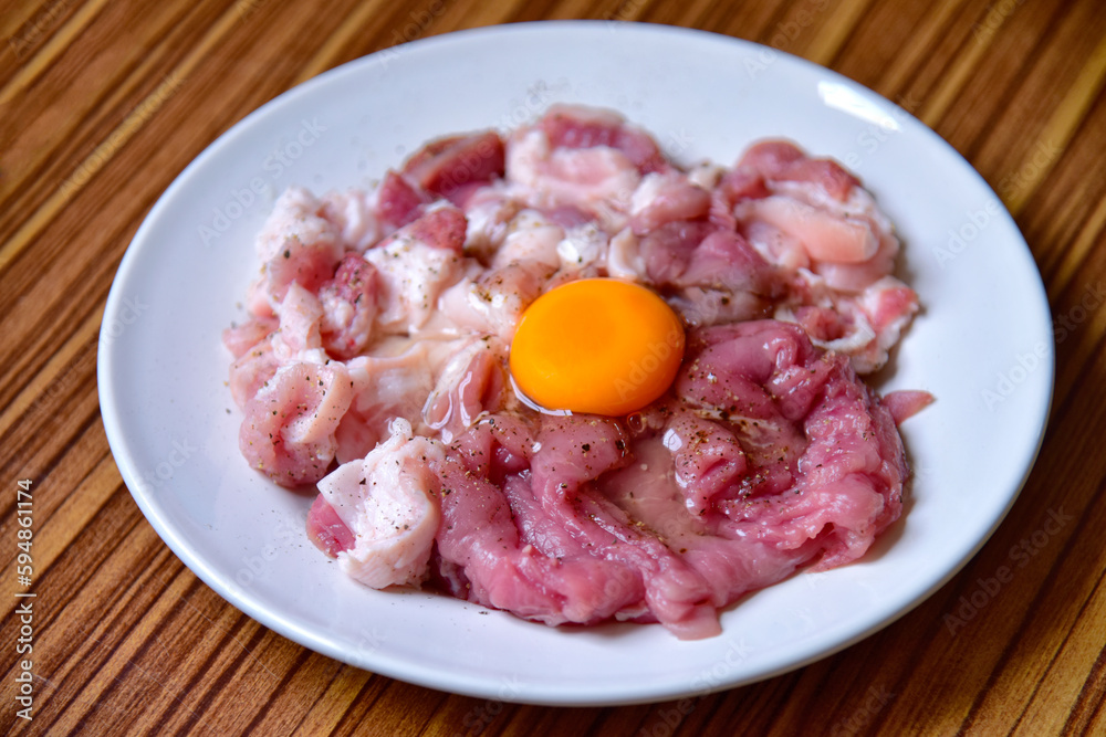 Egg marinated pork made from Suki, beef tartare with egg closeup on a white plate. horizontal Egg marinated pork made from Suki, beef tartare with egg closeup on a white plate. horizontal