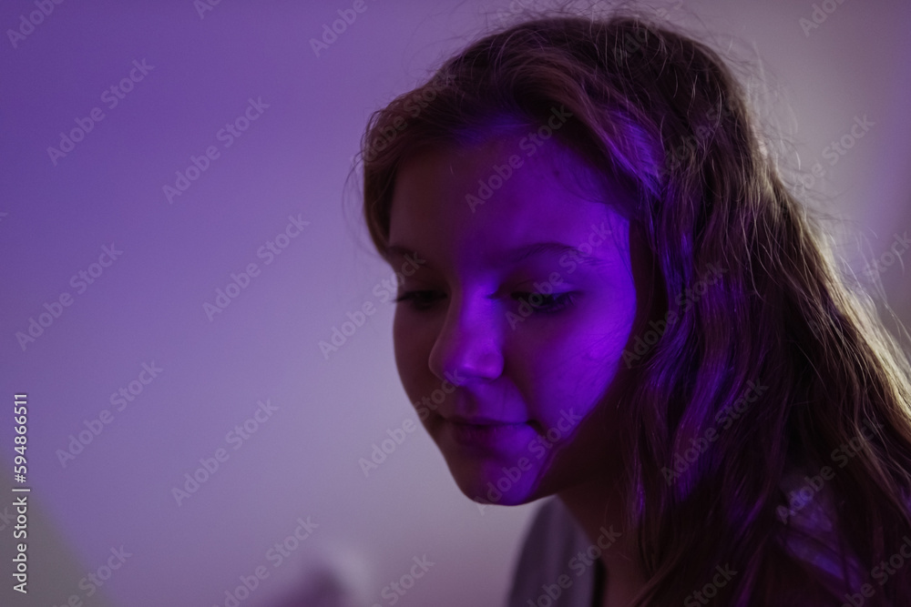 a teenage girl of European appearance with blond hair, sits in a dark room with a colored light turned on, a purple light falls on the girl's face, there is a place for an inscription. a teenage girl of European appearance with blond hair, sits in a dark room with a colored light turned on, a purple light falls on the girl's face, there is a place for an inscription.