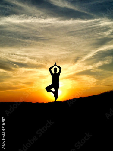 Silhouette young woman practicing yoga on mountain top at amazing sunset.