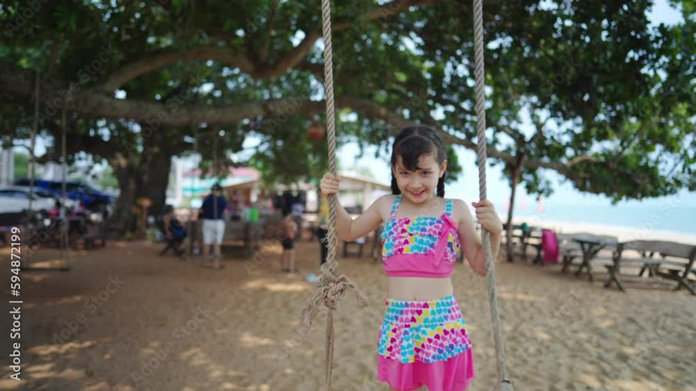 4K Happy Asian family travel ocean on summer holiday vacation. Little Asian child girl kid in swimsuit enjoy and fun outdoor lifestyle playing hanging tree swing at tropical island beach in sunny day.