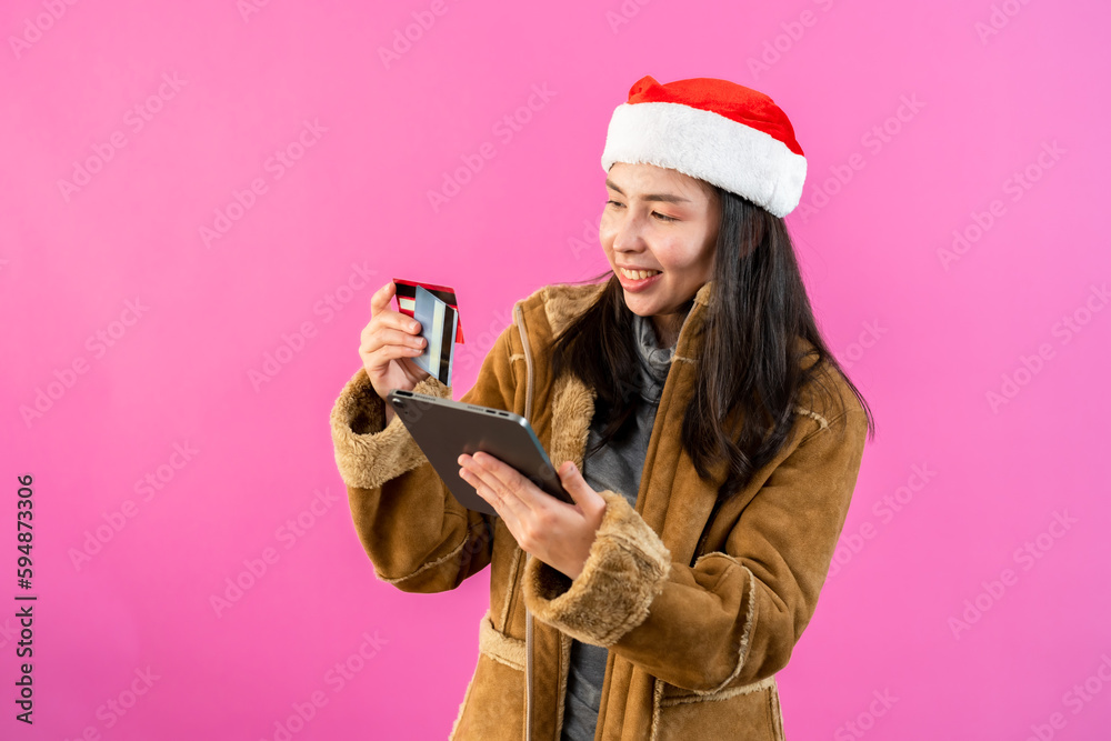 Beautiful girl in long sleeves and christmas hat, hand holding laptop credit card about order online this christmas season, that item has special price, Isolated indoor studio on pink background. Beautiful girl in long sleeves and christmas hat, hand holding laptop credit card about order online this christmas season, that item has special price, Isolated indoor studio on pink background.