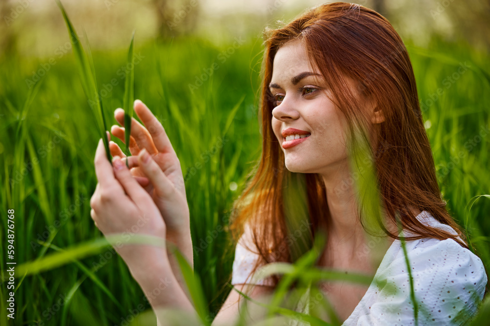 portrait of a cute woman sitting in the grass and smiling joyfully looking at the leaves portrait of a cute woman sitting in the grass and smiling joyfully looking at the leaves