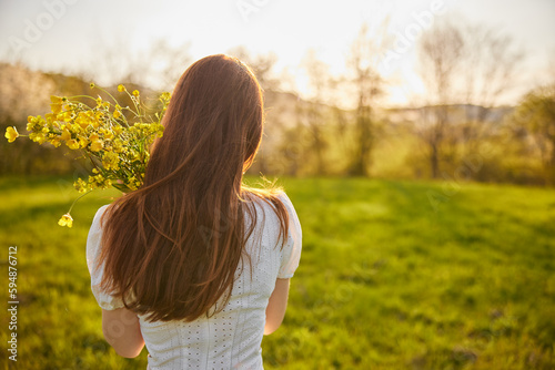 photo from the back of a red-haired woman with a bouquet of flowers in the rays of the setting sun