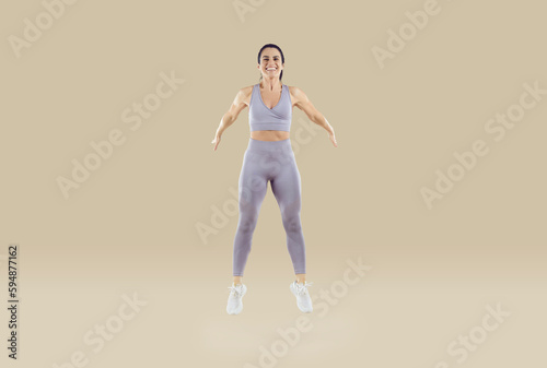 Balance and endurance. Happy strong athletic woman with muscular body trains performing high jumps isolated on beige background. Healthy lifestyle concept. Full length. Banner.