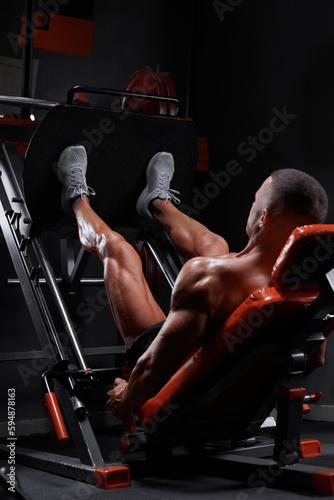 Side view of muscular ethnic male athlete lying on leg press machine and pumping muscles during workout in gym