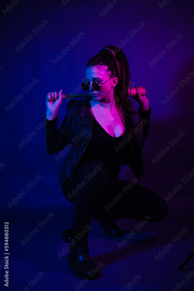 Young woman in a leather jacket in the dark with a machete knife in her hands. Neon light blue pink color. Rogue with melee weapons.