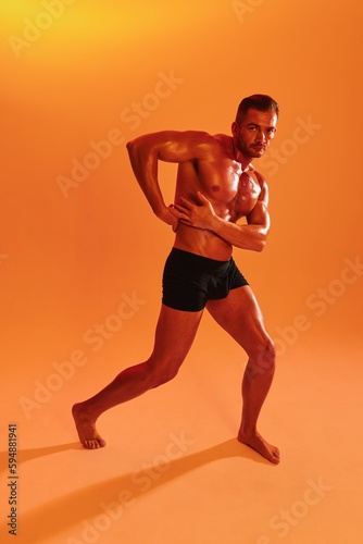 Man bodybuilder boxer muscle workout with naked torso with abs posing in studio. Advertising, sports, active lifestyle, colored yellow light, competition, challenge concept. 
