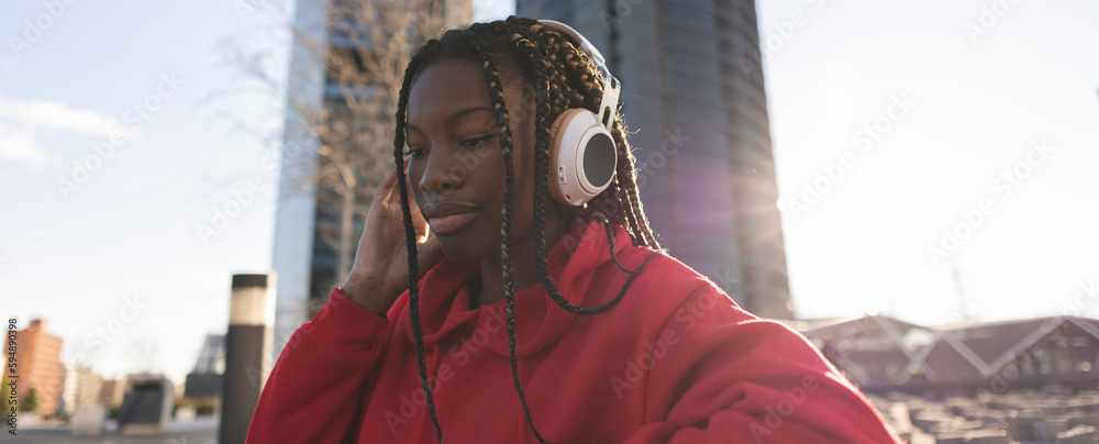 Beautiful black woman with dreadlocks curls hairstyle. Red hooded smiling model. Sexy carefree woman enjoying listening to music in headphones