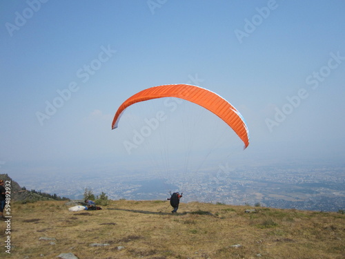 paragliding, orange paraplane, paraglider prepearing to fly on the sky and ground background