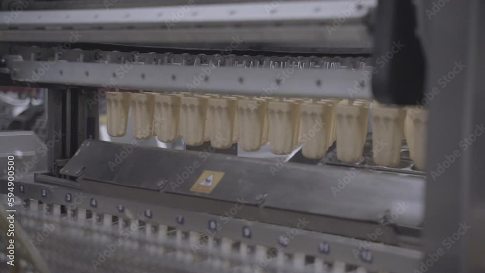 View through machinery of cream vanilla ice cream lollies being made on an industrial food manufacturing line View through machinery of cream vanilla ice cream lollies being made on an industrial food manufacturing line