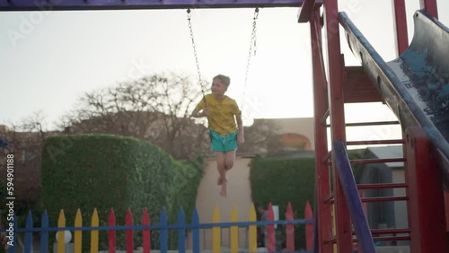 a boy with blond hair is swinging on a swing. a child on the playground