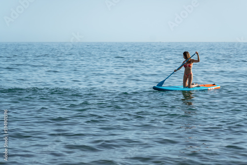 woman on her knees on her surfboard moving through the sea with her oar   © victor