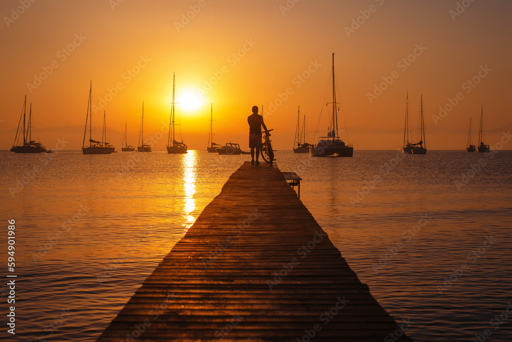 Sunset scene with standing man silhouette with the bicycle on the pier