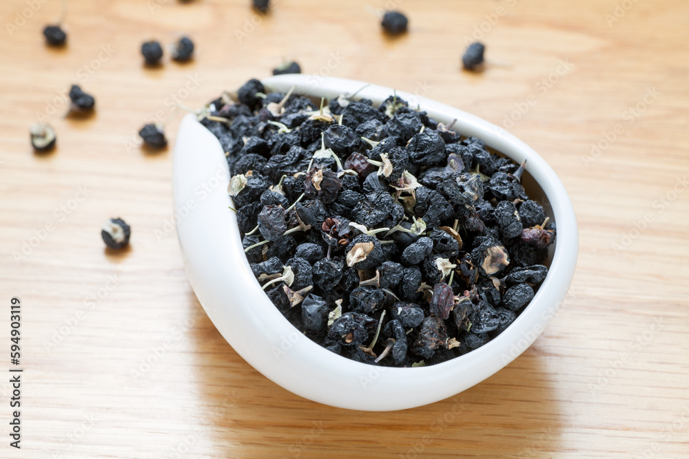black Chinese wolfberry in ceramic spoon on wooden table black Chinese wolfberry in ceramic spoon on wooden table