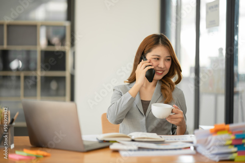 Asian woman standing and talking on the phone with a customer at the office.