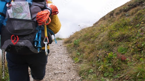 Young man hiker hiking on mountain dirt road with cloudy sky and fog. Yellow jacket, backpack, black beard and beanie. Traveling Dolomites, Italy.