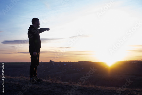 Man at sunset. He points his finger to the sky. Outstretched hand. Evening