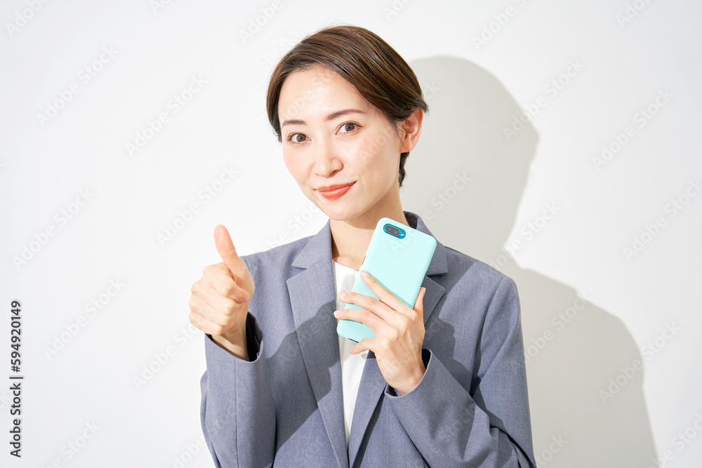スマートフォンを持ってグッドサインするビジネスウーマン 白背景 スマートフォンを持ってグッドサインするビジネスウーマン 白背景