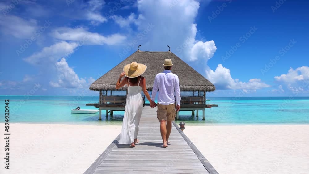 A happy holiday couple in white summer clothing walks down a wooden pier  in the Maldives islands, Indian Ocean