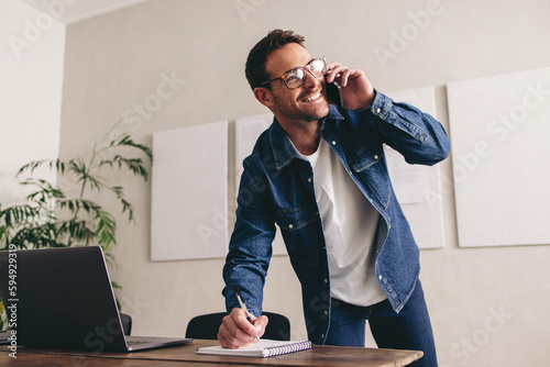 Smiling businessman writing notes during a phone call