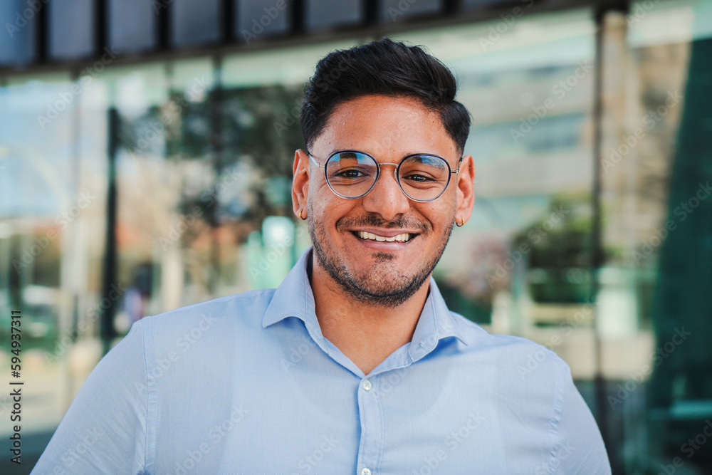 close up portrait of hispanic young entrepreneur smiling and looking at camera at workspace. Front view of one latin happy employee office worker with glasses and successful attitude standing outdoors close up portrait of hispanic young entrepreneur smiling and looking at camera at workspace. Front view of one latin happy employee office worker with glasses and successful attitude standing outdoors