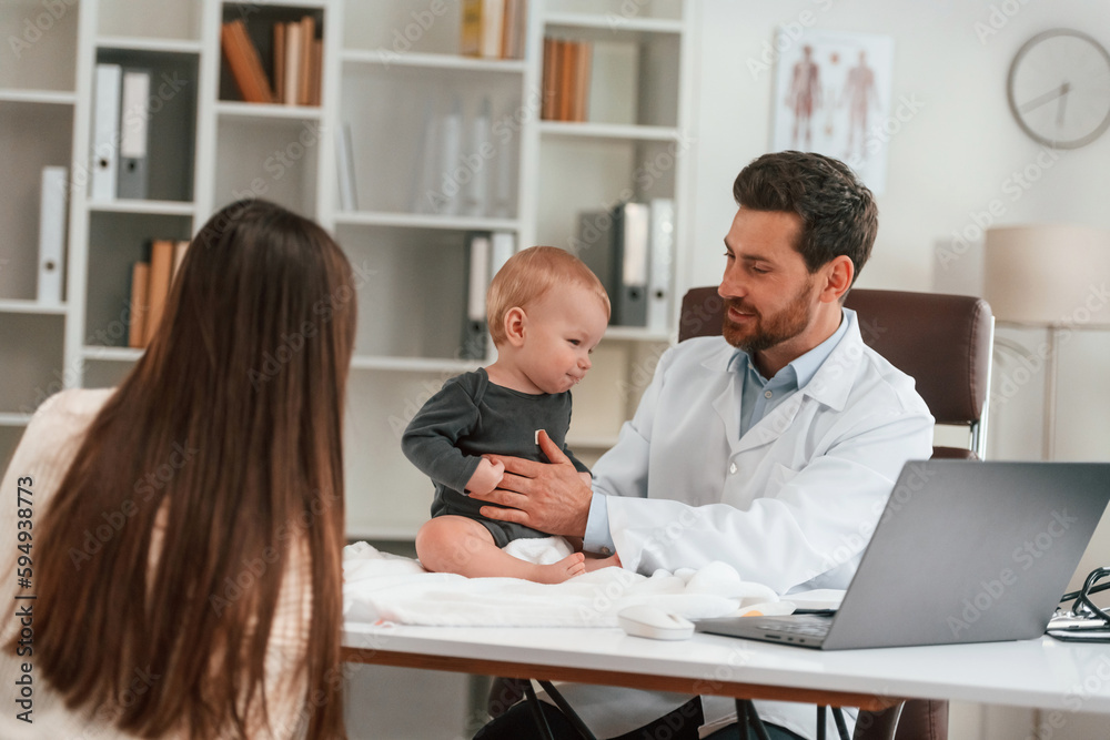 Having consultation. With baby and mother. Doctor in formal clothes is working in the cabinet